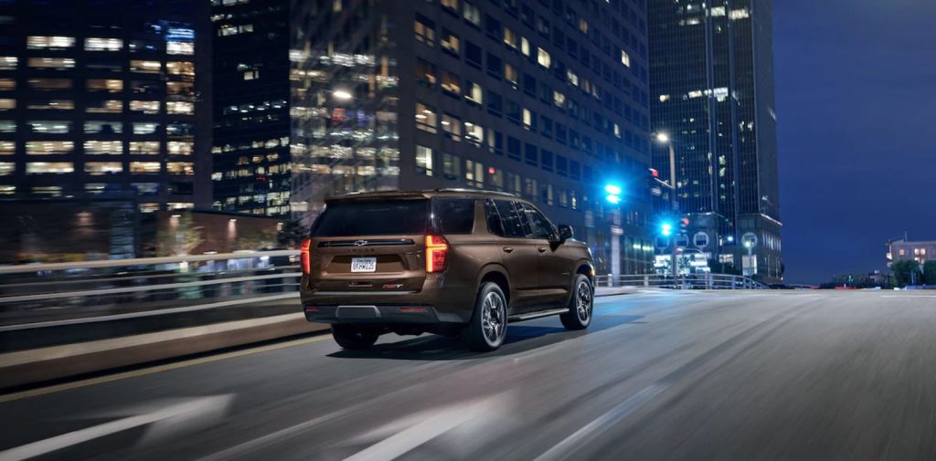 A brown 2022 Chevrolet Tahoe shown from the back as it's driving down a city road at night.