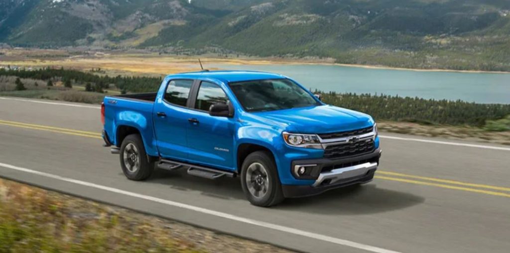 A blue 2022 Chevrolet Colorado driving down a road near a lake.