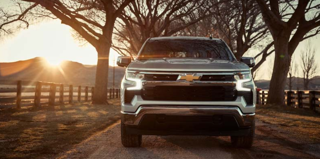 A gray 2023 Chevy Silverado 1500 driving towards us in perspective with the sunset behind it.