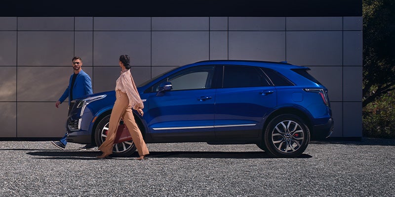 A blue 2024 Cadillac XT5 and its owners walking away.