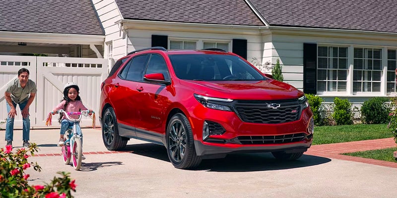 A red 2024 Chevrolet Equinox parked in a driveway, the owner and their daughter are riding a bike.