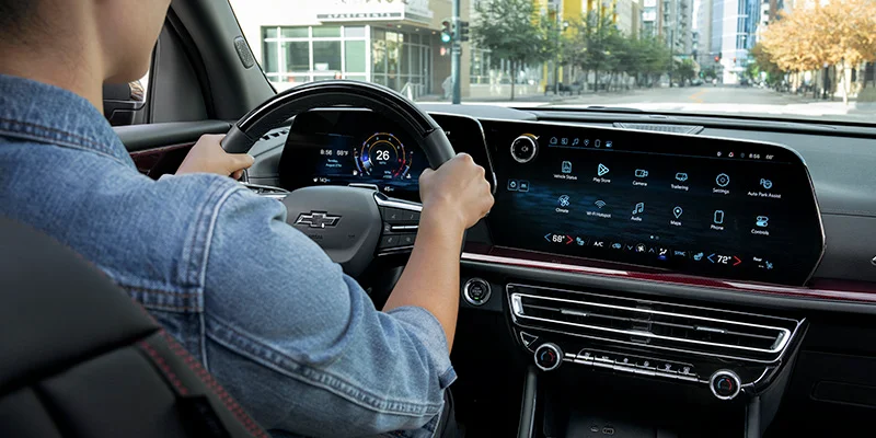 A person driving a Chevrolet car, with a modern dashboard and large touchscreen display visible in the cabin.