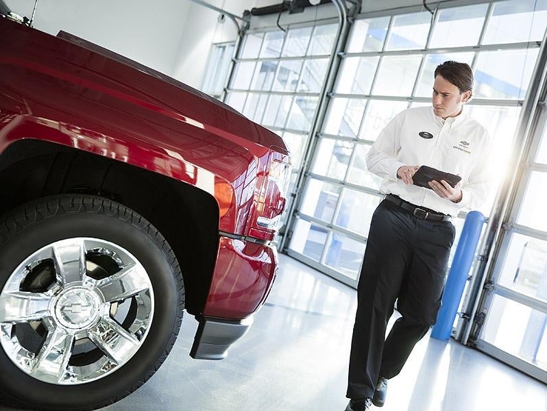 Dealership associate checks a red pickup truck with a tablet.